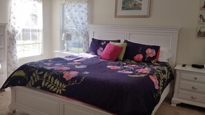 Um quarto com cama, mesa de cabeceira, cômoda e janela com cortinas.