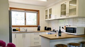 A modern kitchen with white cabinets, a wooden countertop, a built-in microwave, and a window with a view of trees.