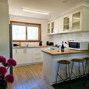 A modern kitchen with white cabinets, a wooden countertop, a built-in microwave, and a window with a view of trees.