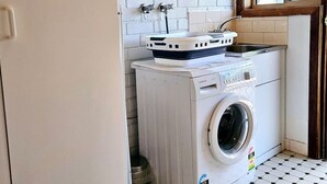A compact laundry area with a washing machine and a drying rack, white tiled walls, and a window.