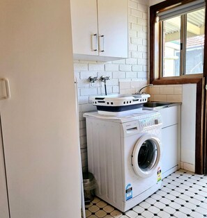 A compact laundry area with a washing machine and a drying rack, white tiled walls, and a window.