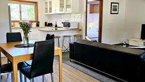 A modern kitchen with white cabinets, a dining table with chairs, and a black sofa.