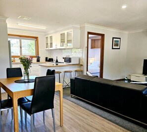 A modern kitchen with white cabinets, a dining table with chairs, and a black sofa.