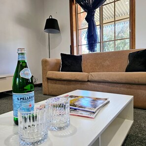 A living room with a sofa, a table with a magazine, a bottle of S. Pellegrino sparkling water, and a glass.