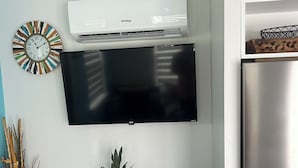Eine Küche mit einem Flachbildfernseher über einem schwarzen Schrank, einem Edelstahlkühlschrank und einer wandmontierten Klimaanlage.