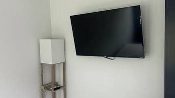 Una habitación con una televisión de pantalla plana montada, una lámpara de pie de madera y una pared blanca.