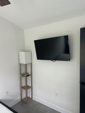 A room with a mounted flat-screen TV, a wooden floor lamp, and a white wall.