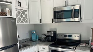 Eine moderne Küche mit weißen Schränken, Edelstahlgeräten, einer Mikrowelle, einer Kaffeemaschine und einem Kühlschrank.