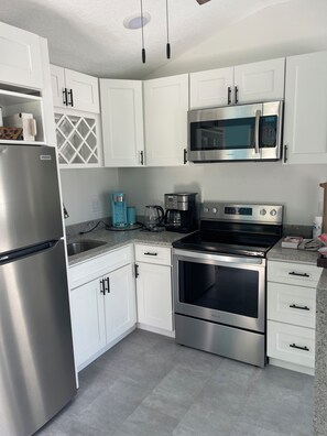 A modern kitchen with white cabinets, stainless steel appliances, a microwave, a coffee maker, and a refrigerator.