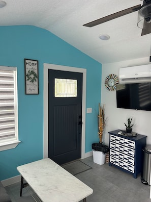 A modern kitchen with a black door, a dining table, a wall-mounted TV, and a ceiling fan.