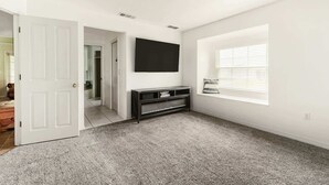 Ein Zimmer mit weißer Tür, einer schwarzen Unterhaltungseinheit, einem Fenster mit Jalousien und einem Teppichboden.