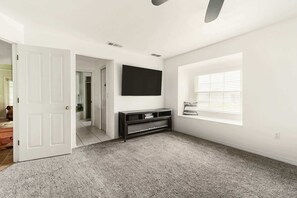 A room with a white door, a black entertainment unit, a window with blinds, and a carpeted floor. - Heated Pool Home with Foosball/BBQ/Kids Playroom (Englewood)