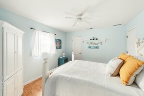 Un dormitorio con cama, ventilador de techo, un cartel que dice 'WELCOME' y una pequeña mesa con lámpara.