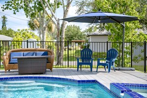 A poolside area with a wicker sofa, two Adirondack chairs, a table, and a blue umbrella. - Heated Pool Home with Foosball/BBQ/Kids Playroom (Englewood)