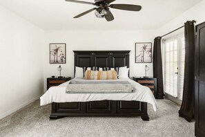 Una camera da letto con un letto in legno scuro, biancheria da letto bianca, due comodini, una ventola a soffitto e una finestra con persiane.