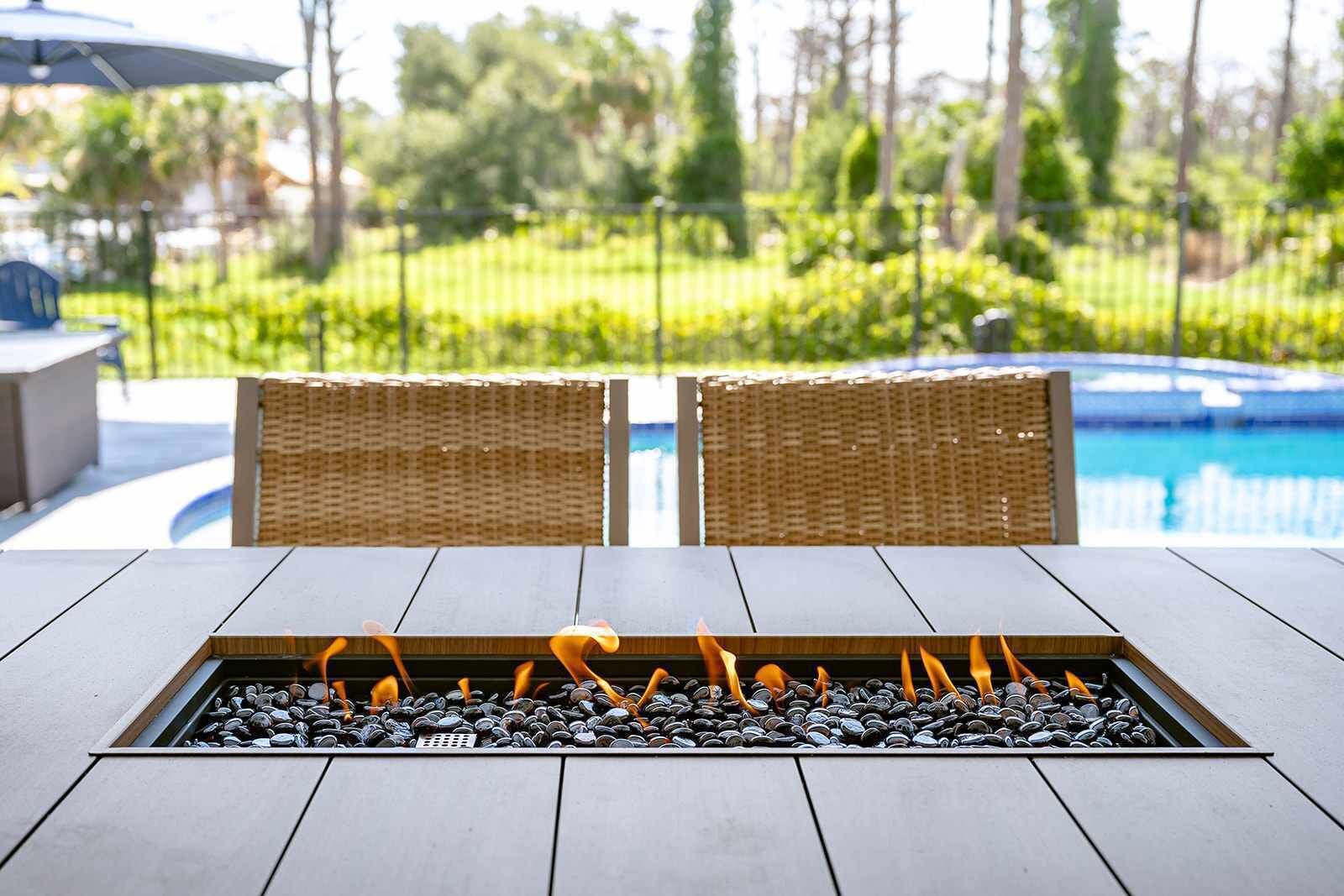 A fire feature with a stone surround, two wicker chairs, and a pool in the background.