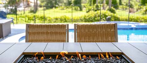 A fire feature with a stone surround, two wicker chairs, and a pool in the background.