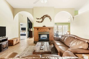 A living room with a fireplace, a leather sofa, a coffee table, and a television. - Heated Pool Home with Foosball/BBQ/Kids Playroom (Englewood)
