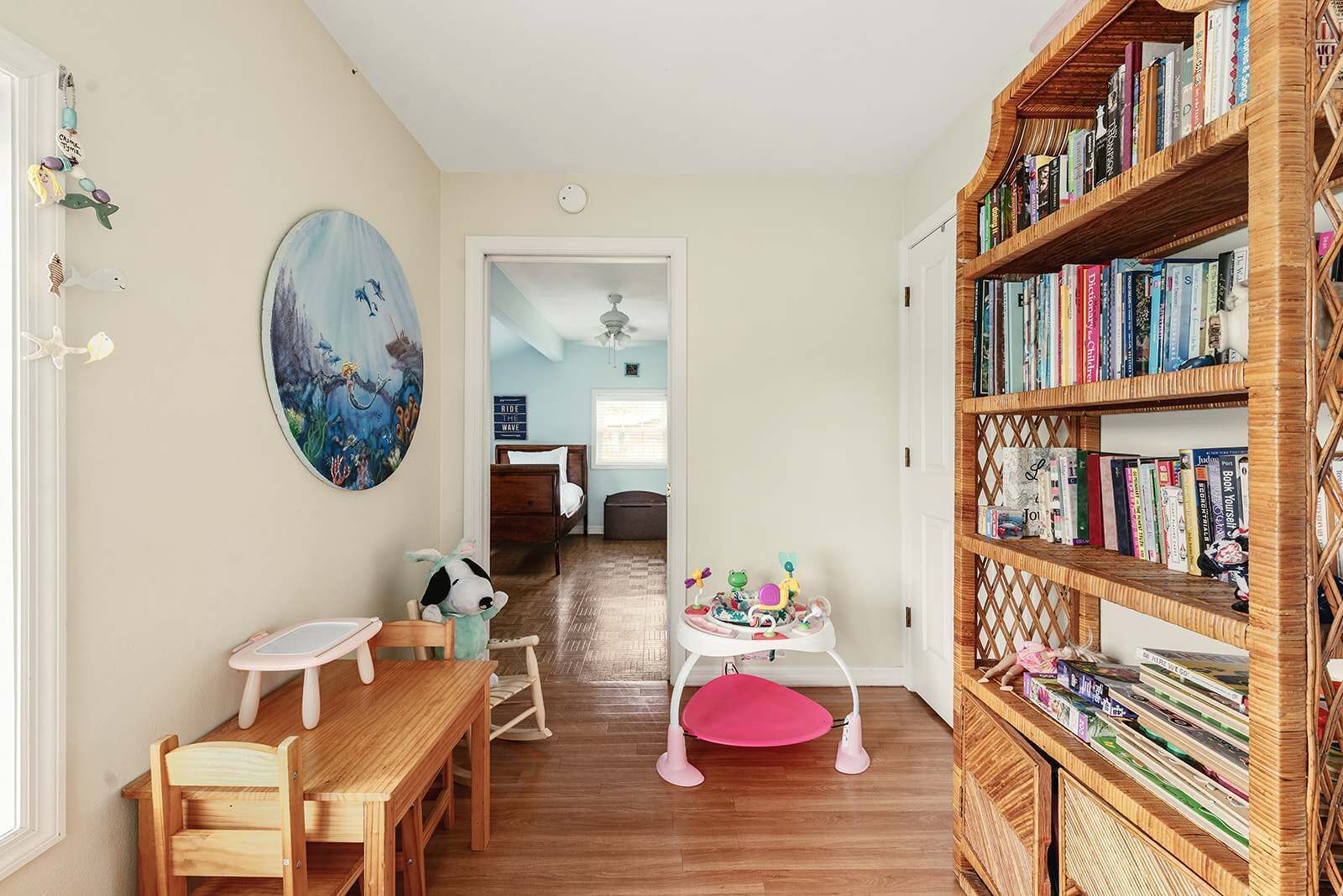 A child's room with a wooden bookshelf, a painting, and a play area with a small table and chairs.