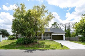 A single-story house with a garage, surrounded by a well-maintained lawn and mature trees. - Heated Pool Home with Foosball/BBQ/Kids Playroom (Englewood)