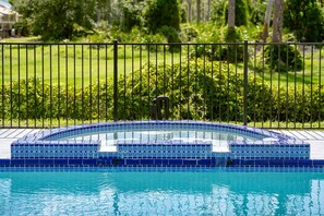 Una piscina con borde de azulejos, rodeada por una valla metálica y abundante vegetación.
