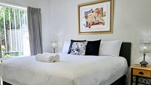 A neatly made bed with white linens and two pillows, a bedside table with a lamp, and a framed picture on the wall. - Garden Retreat on Orr – Your Peaceful Hideaway (Shepparton)