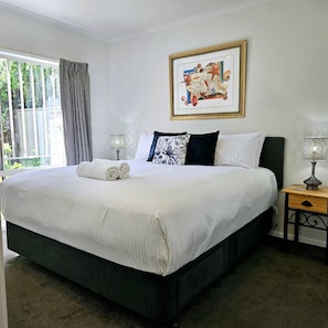 A neatly made bed with white linens and two pillows, a bedside table with a lamp, and a framed picture on the wall. - Garden Retreat on Orr – Your Peaceful Hideaway (Shepparton)