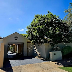 A building with a garage entrance, a tree in front, and a clear sky. - Garden Retreat on Orr – Your Peaceful Hideaway (Shepparton)