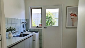 A compact kitchen with a built-in dishwasher, a window with a view of greenery, and a framed picture on the wall. - Garden Retreat on Orr – Your Peaceful Hideaway (Shepparton)