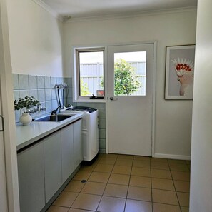 A compact kitchen with a built-in dishwasher, a window with a view of greenery, and a framed picture on the wall. - Garden Retreat on Orr – Your Peaceful Hideaway (Shepparton)