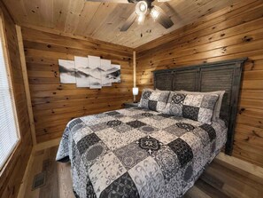 A wooden-paneled bedroom with a bed, a wall-mounted light, and a ceiling fan.