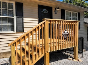 A wooden deck with a caution sign for bear sightings, a black door, and a house number 1148.
