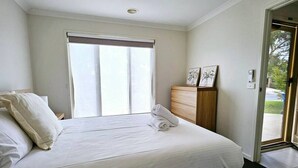 Ein Schlafzimmer mit Bett, Fenster, Kommode und einer Tür, die nach draußen führt.