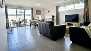 Ein geräumiges Wohnzimmer mit einer Couch, einem Fernseher und einem Esstisch mit Stühlen.