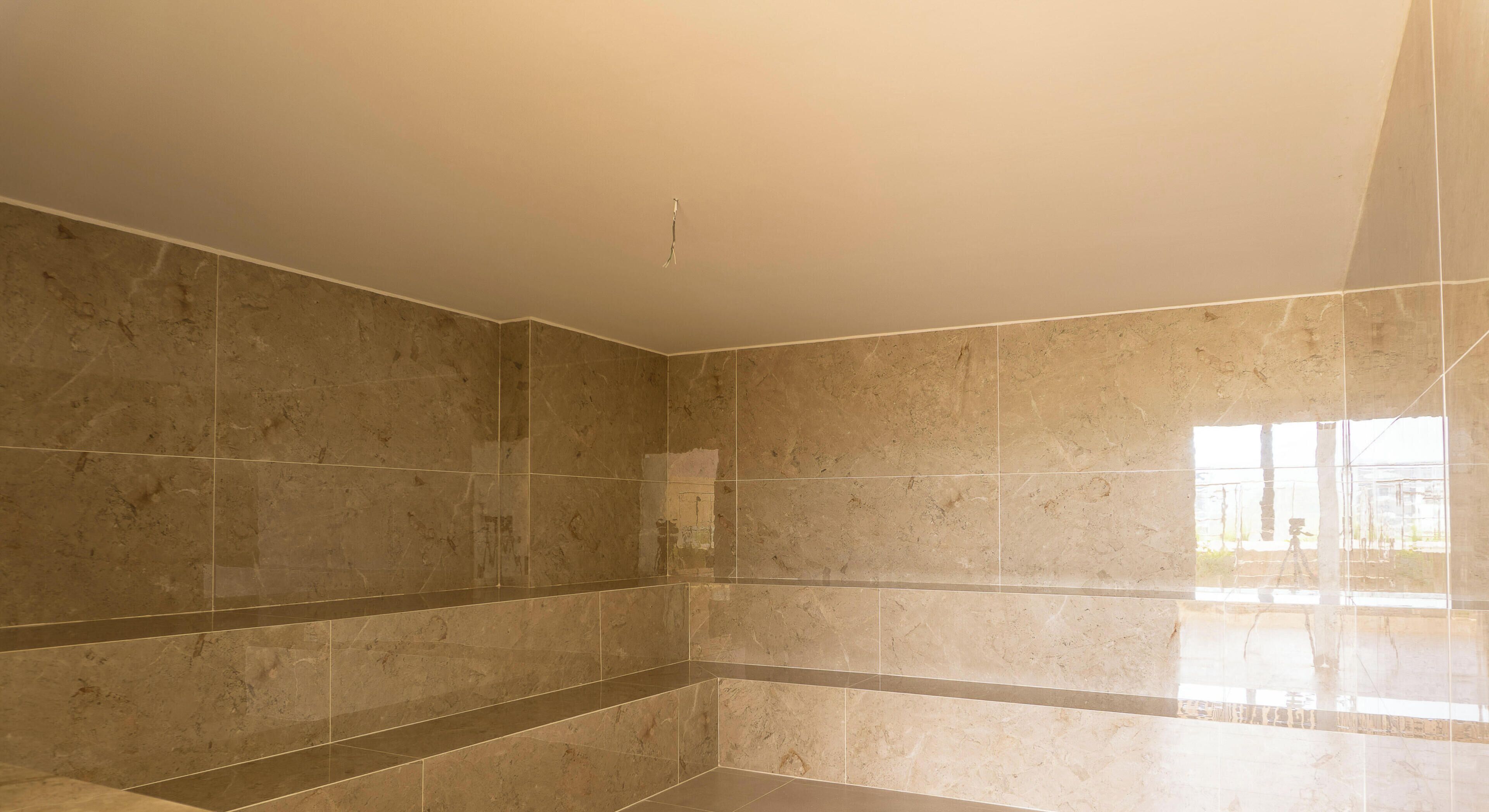 A bathroom with large marble tiles, a white ceiling, and a visible window.