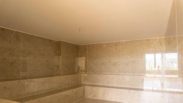 A bathroom with large marble tiles, a white ceiling, and a visible window.