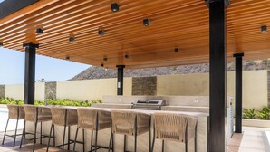 An outdoor bar area with a pool, bar stools, and a grill.