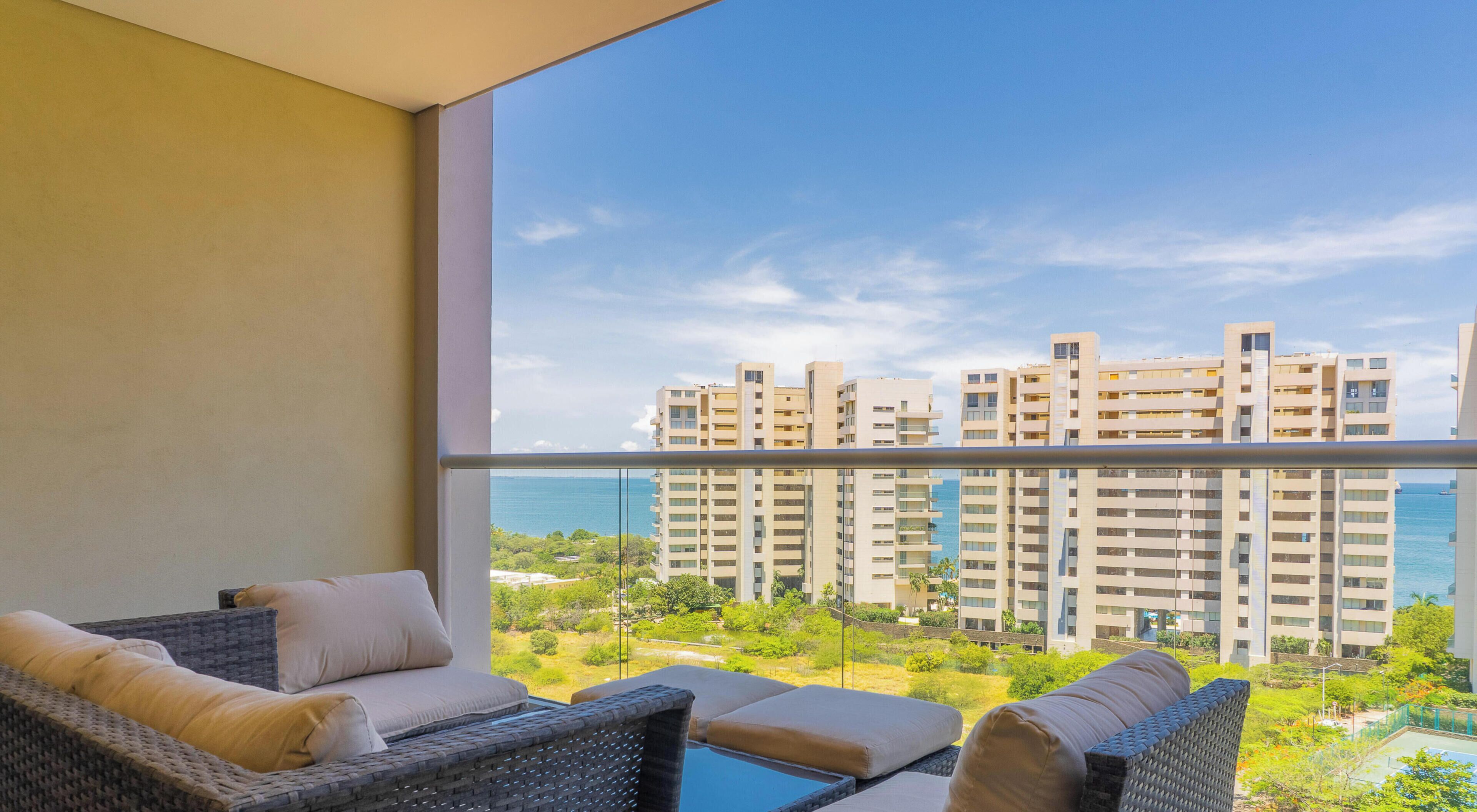 A balcony with wicker furniture and a view of high-rise buildings and a body of water.