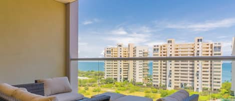 A balcony with wicker furniture and a view of high-rise buildings and a body of water.