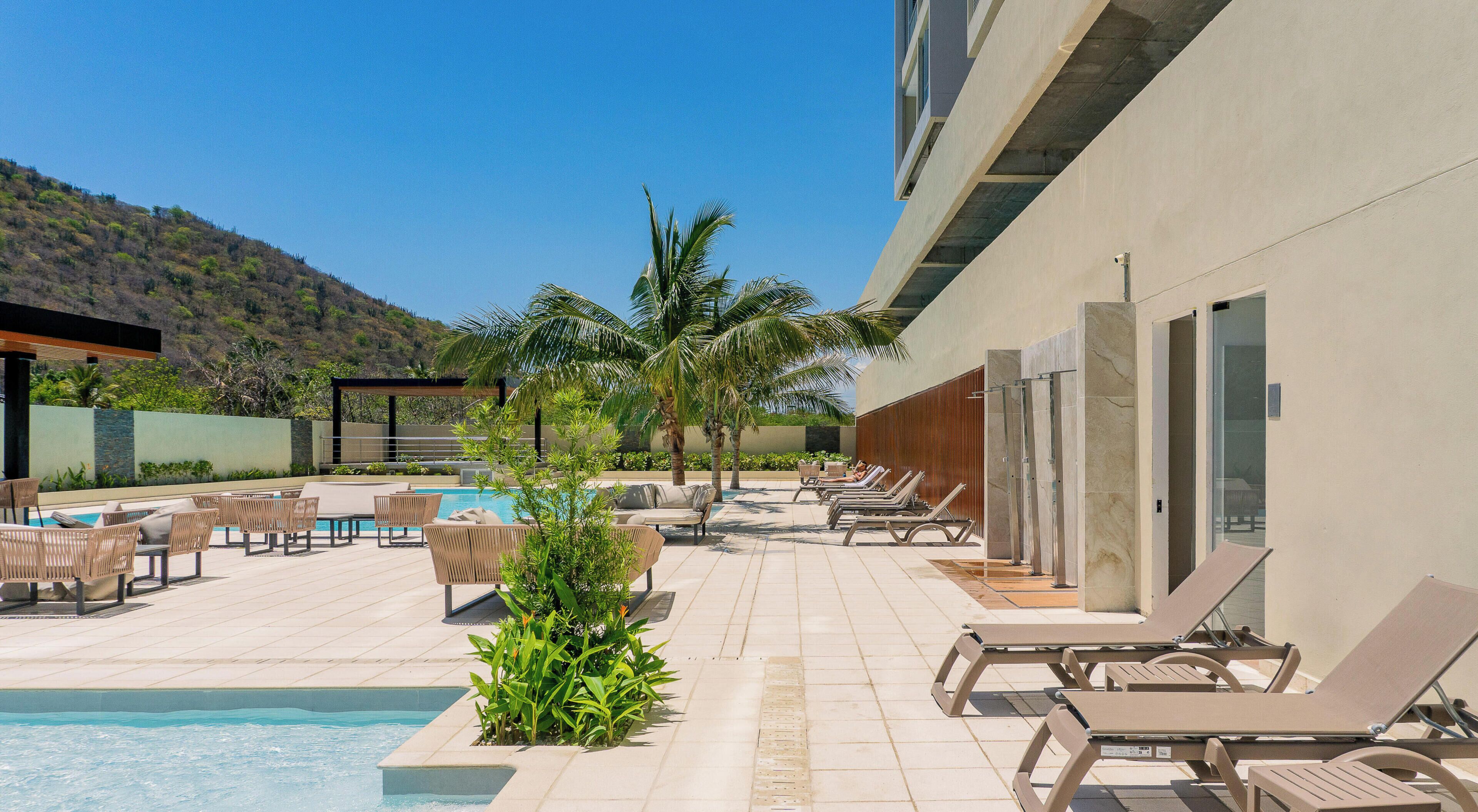 A poolside area with lounge chairs, a swimming pool, and a view of a hillside.