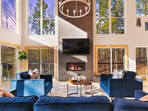 A spacious living room with a fireplace, large windows, and a modern chandelier. - Modern and Luxury • Mini Golf • Hot Tub • Hot Tub (Broken Bow)