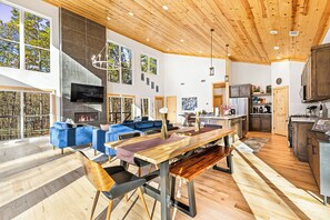 A spacious living area with a large wooden dining table, blue sofas, and a fireplace. - Fall Promo! Modern • Mini Golf • Hot Tub • Hot Tub (Broken Bow)