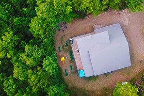 An aerial view of a property with a large building, a fenced yard, and dense surrounding trees. - Modern and Luxury • Mini Golf • Hot Tub • Hot Tub (Broken Bow)