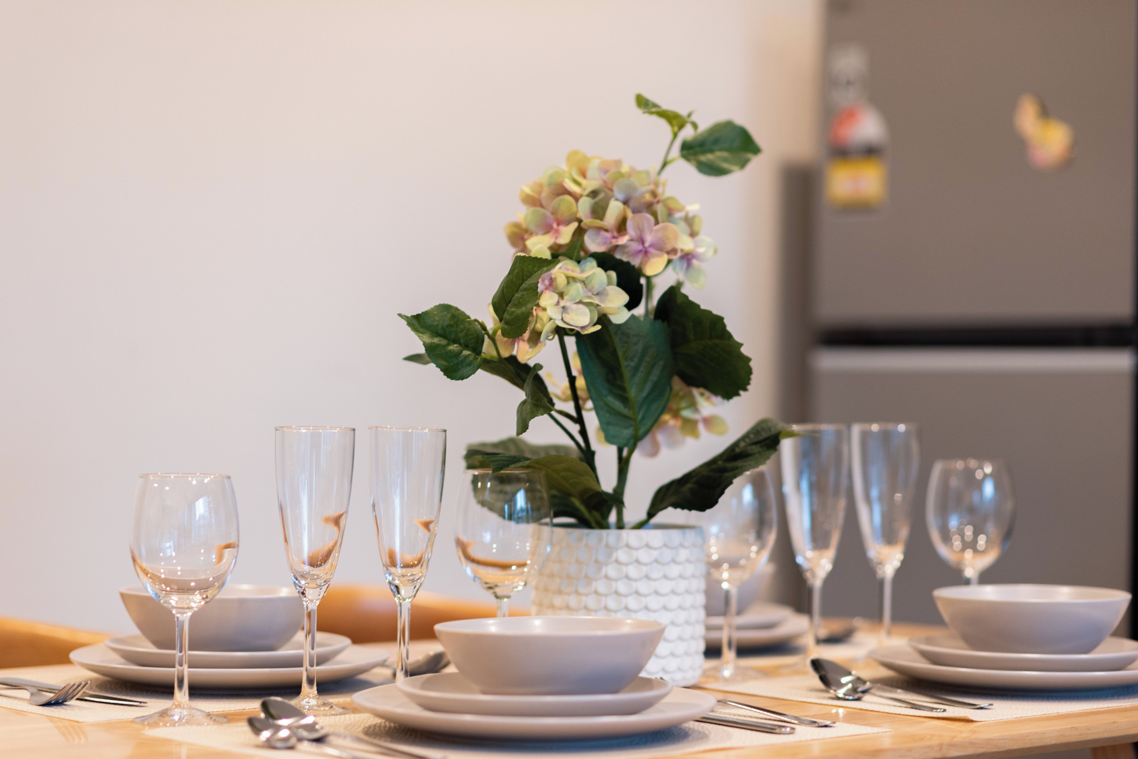 A dining table set with multiple plates, bowls, and wine glasses, with a potted plant in the center.