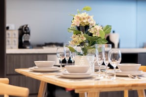 A dining table set with white plates, bowls, and wine glasses, with a vase of flowers in the center.
