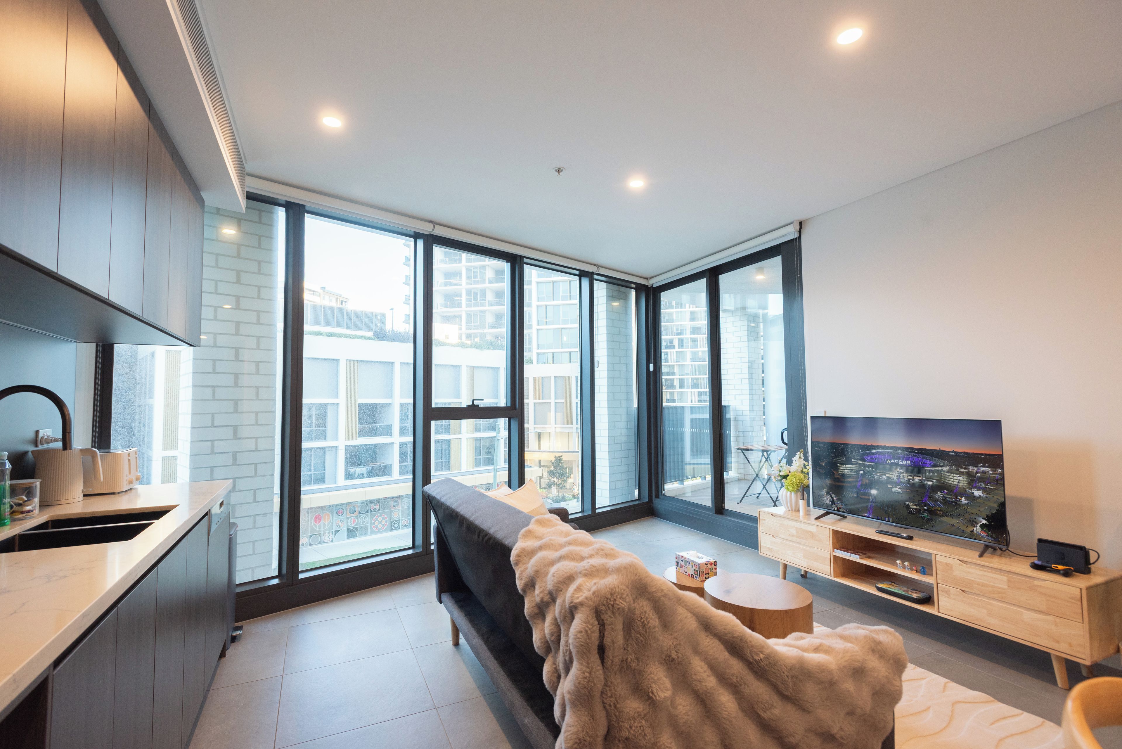 A modern living room with a sofa, a TV, and a large window offering a city view.