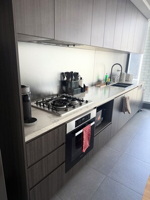 A modern kitchen with a built-in stove, oven, and dishwasher. - Olympic Park Stadium Gym, Pool & Parking (Lidcombe)