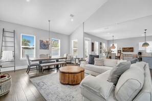 A spacious living room with a dining area, a kitchen, and a large window providing natural light. - 🦩Book Me Baby! High Tide in Miramar Beach ~ Golf Cart Included🦩 (Miramar Beach)