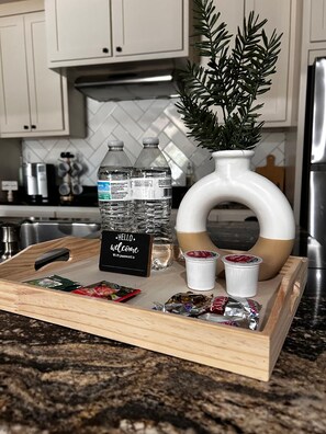 Una bandeja con botellas de agua, un cartel, bocadillos y una planta decorativa en una cocina.
