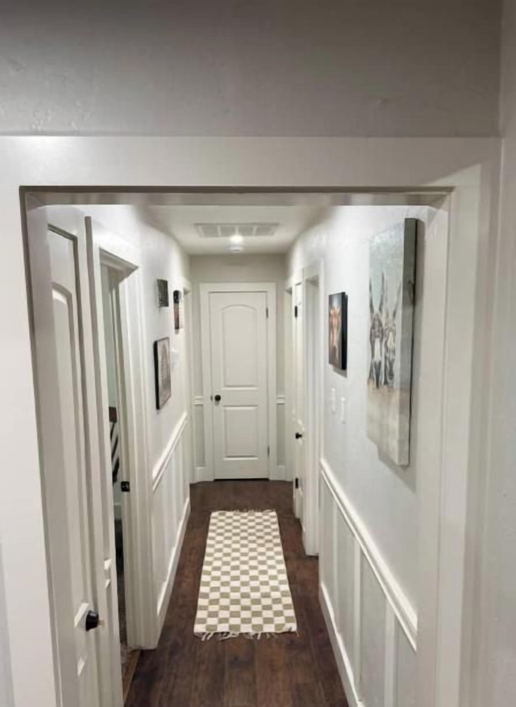 A hallway with white walls, a checkered floor, and framed pictures on the walls.